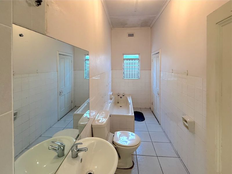 A dated bathroom featuring a built-in bathtub, pedestal basin, and toilet, finished with white ceramic wall and floor tiles.