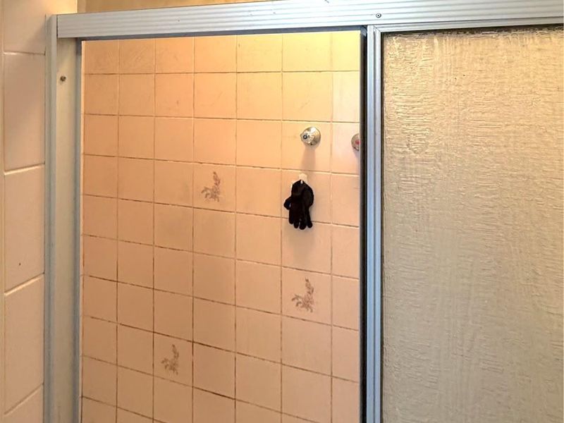 A dated shower stall featuring original tiled walls and flooring, requiring renovation to update the finishes and improve the overall condition of the bathroom.