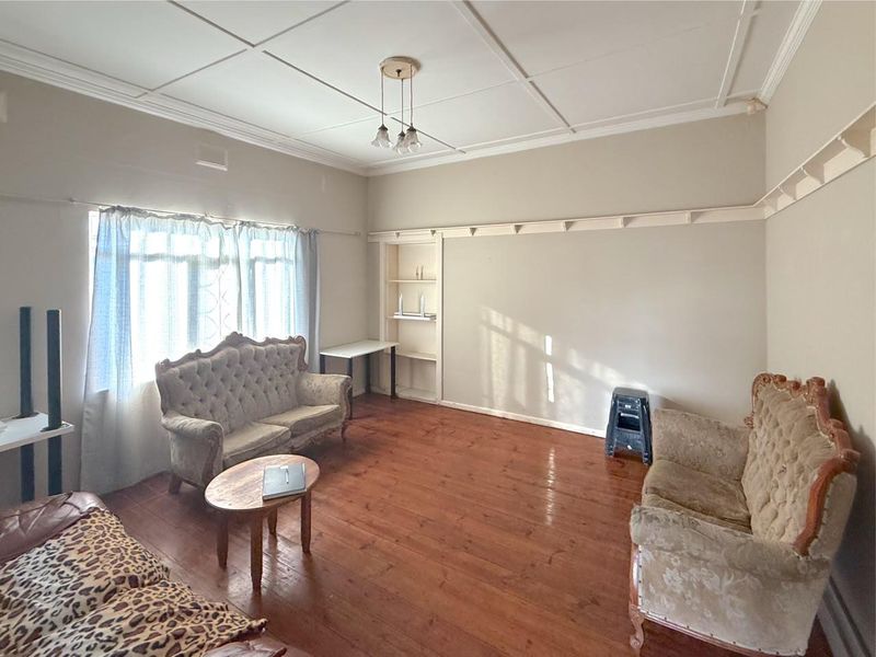 A living room featuring original timber flooring, decorative ceiling panels, and built-in shelving, offering a classic foundation for renovation.