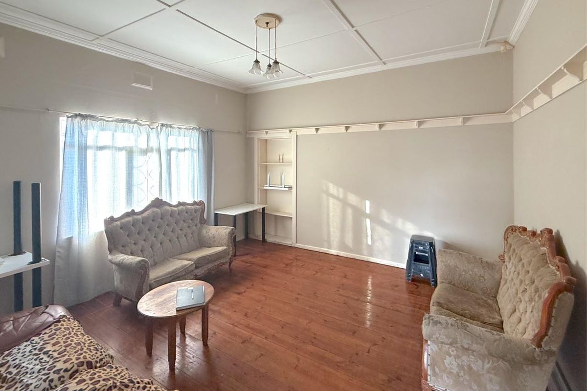 A living room featuring original timber flooring, decorative ceiling panels, and built-in shelving, offering a classic foundation for renovation.