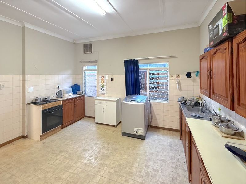 A functional kitchen featuring wooden cabinetry, a built-in oven, and a stainless steel sink, with tiled splashbacks and security-barred windows.