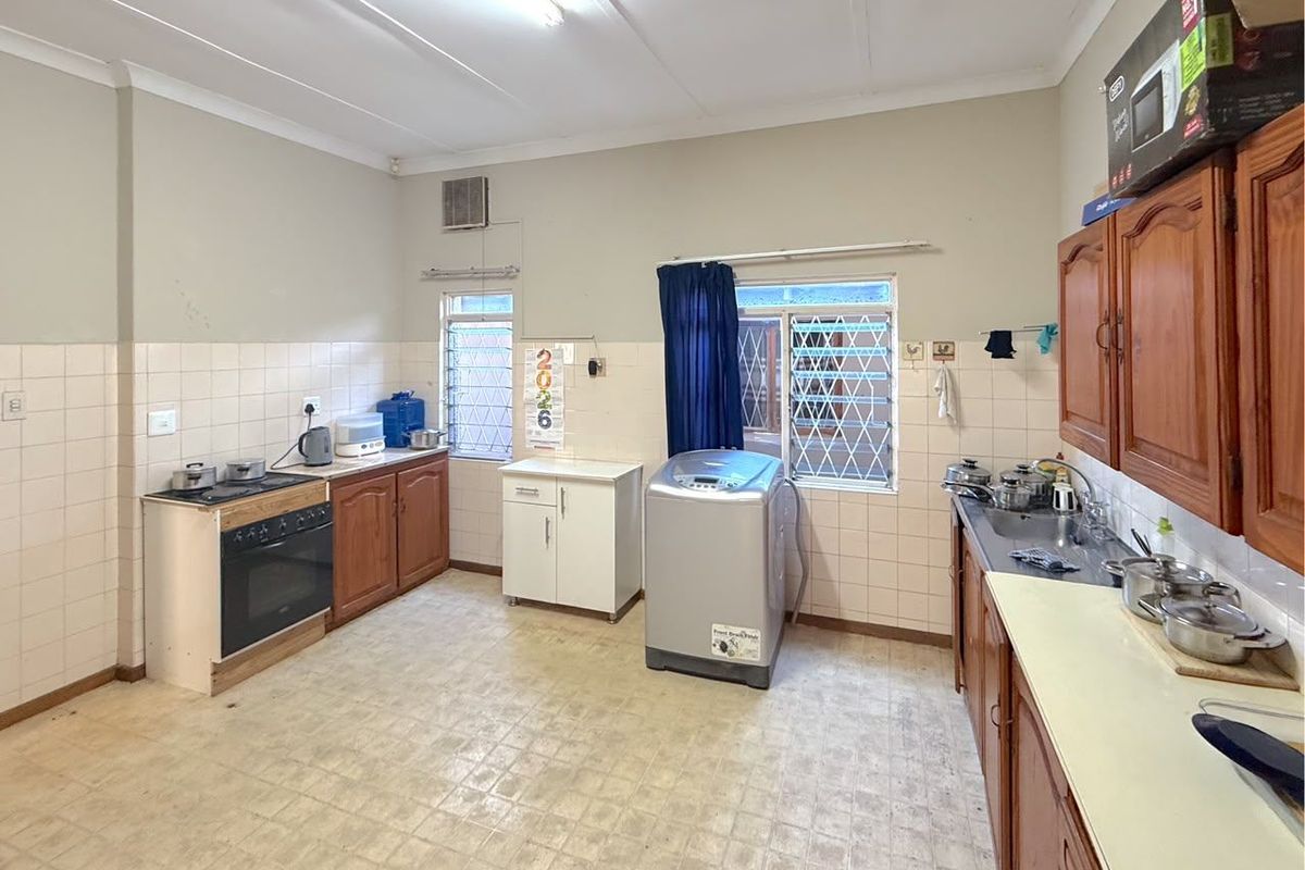 A functional kitchen featuring wooden cabinetry, a built-in oven, and a stainless steel sink, with tiled splashbacks and security-barred windows.