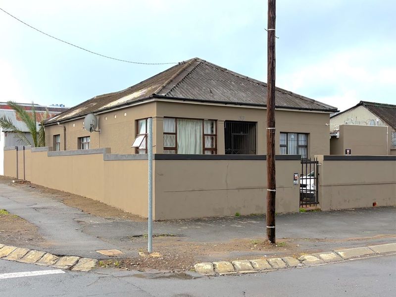 Street-facing view of a single-story house featuring a perimeter wall, security gate, and tiled roof structure.