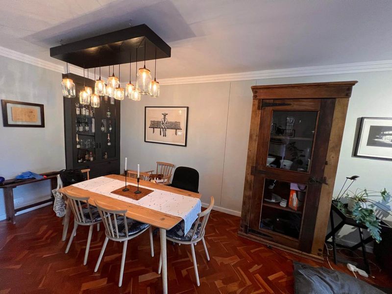 A dining room featuring classic parquet flooring, crown molding, and a built-in display cabinet, illuminated by a modern multi-pendant light fixture.