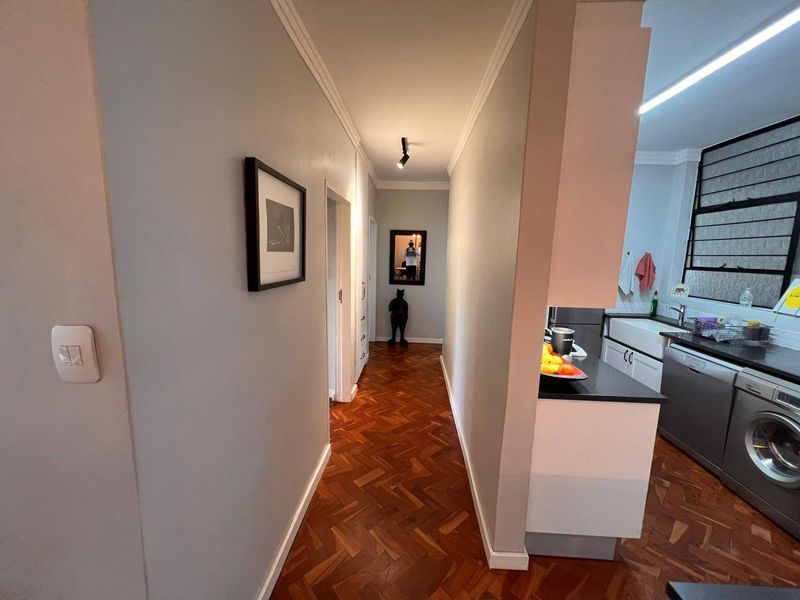 A well-maintained hallway featuring classic herringbone parquet flooring and cove cornicing, providing a seamless transition into the adjacent kitchen area.