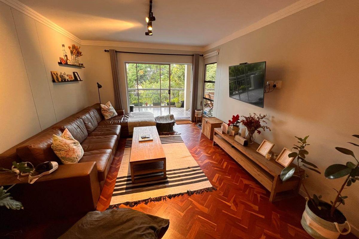 A cozy living room featuring classic herringbone parquet flooring, track lighting, and a large sliding glass door leading to an outdoor balcony.
