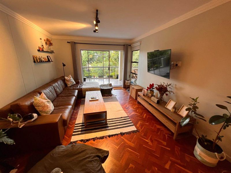 A cozy living room featuring classic herringbone parquet flooring, track lighting, and a large sliding glass door leading to an outdoor balcony.
