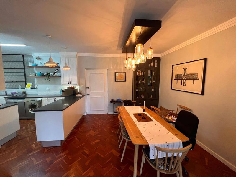 Open-plan living and dining area featuring classic herringbone parquet flooring, modern white kitchen cabinetry with stone countertops, and elegant pendant lighting.