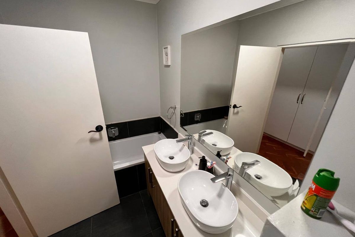 Modern bathroom featuring a double vanity with vessel sinks, a large wall mirror, and a built-in bathtub with dark tiled accents.