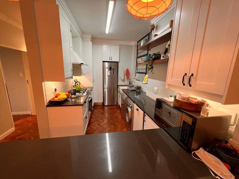 Modern kitchen featuring white shaker-style cabinetry, dark stone countertops, integrated appliances, and elegant herringbone parquet flooring.