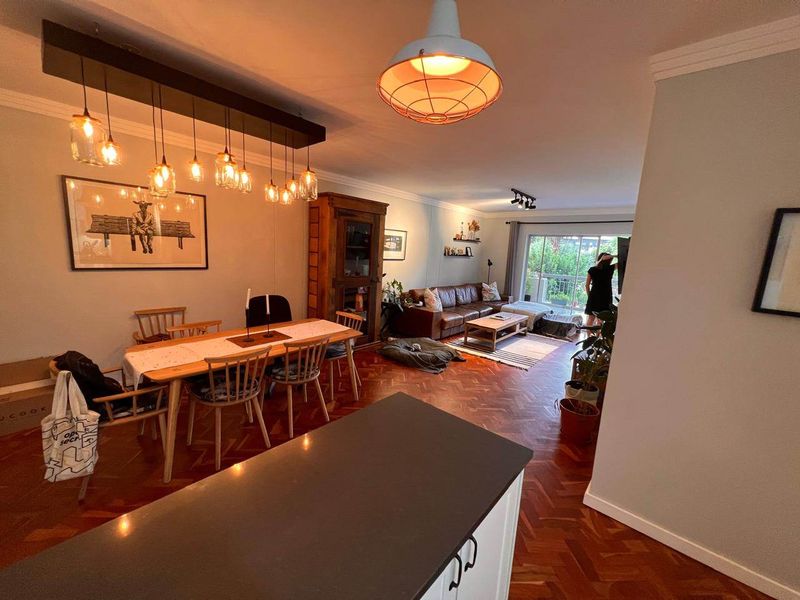 Spacious open-plan living and dining area featuring classic herringbone parquet flooring, modern pendant lighting, and seamless access to an outdoor balcony.