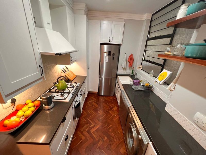 Modern galley kitchen featuring shaker-style cabinetry, stone countertops, a farmhouse sink, gas hob, and elegant herringbone timber flooring.