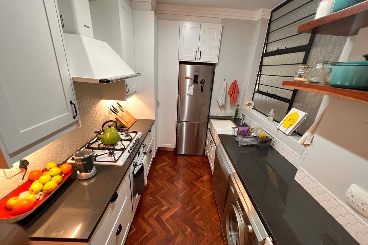 Modern galley kitchen featuring shaker-style cabinetry, stone countertops, a farmhouse sink, gas hob, and elegant herringbone timber flooring.