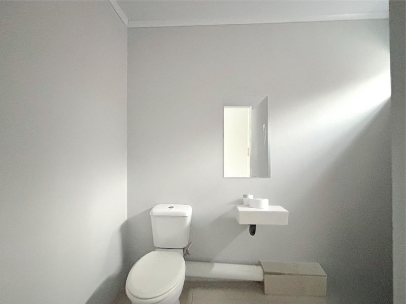 A minimalist guest bathroom featuring a white toilet and a simple wall-mounted basin with a mirror.