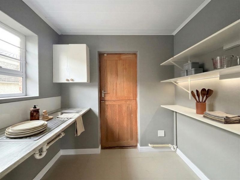 A clean and functional scullery featuring a stainless steel sink, built-in cabinetry, open shelving, and a classic timber door.