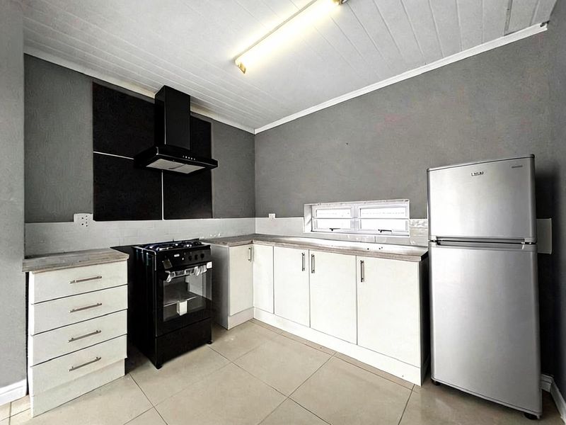 A functional kitchen featuring white cabinetry, a black extractor fan, a gas stove, and tiled flooring with a neutral grey wall finish.