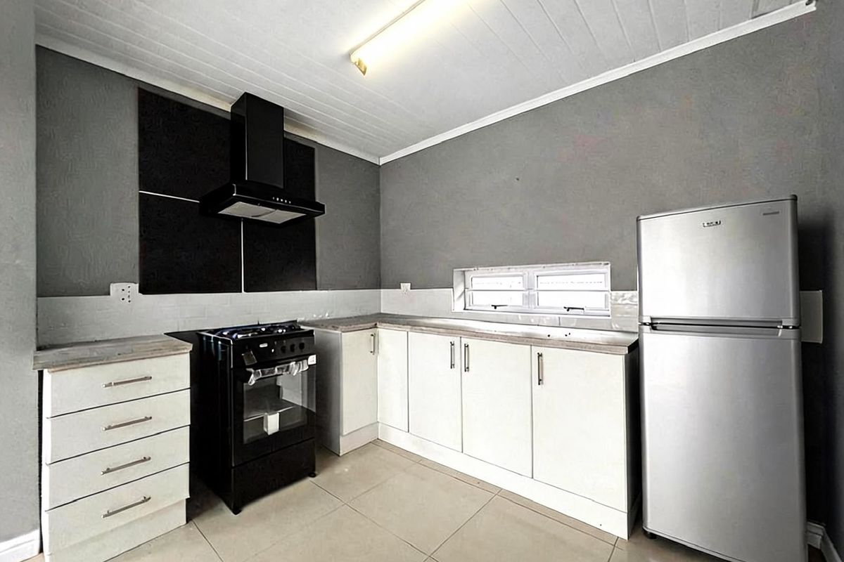 A functional kitchen featuring white cabinetry, a black extractor fan, a gas stove, and tiled flooring with a neutral grey wall finish.