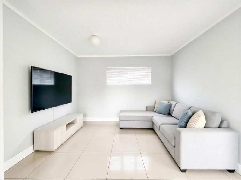 A bright and modern living room featuring neutral tiled flooring, a tongue and groove ceiling, and clean finishes.