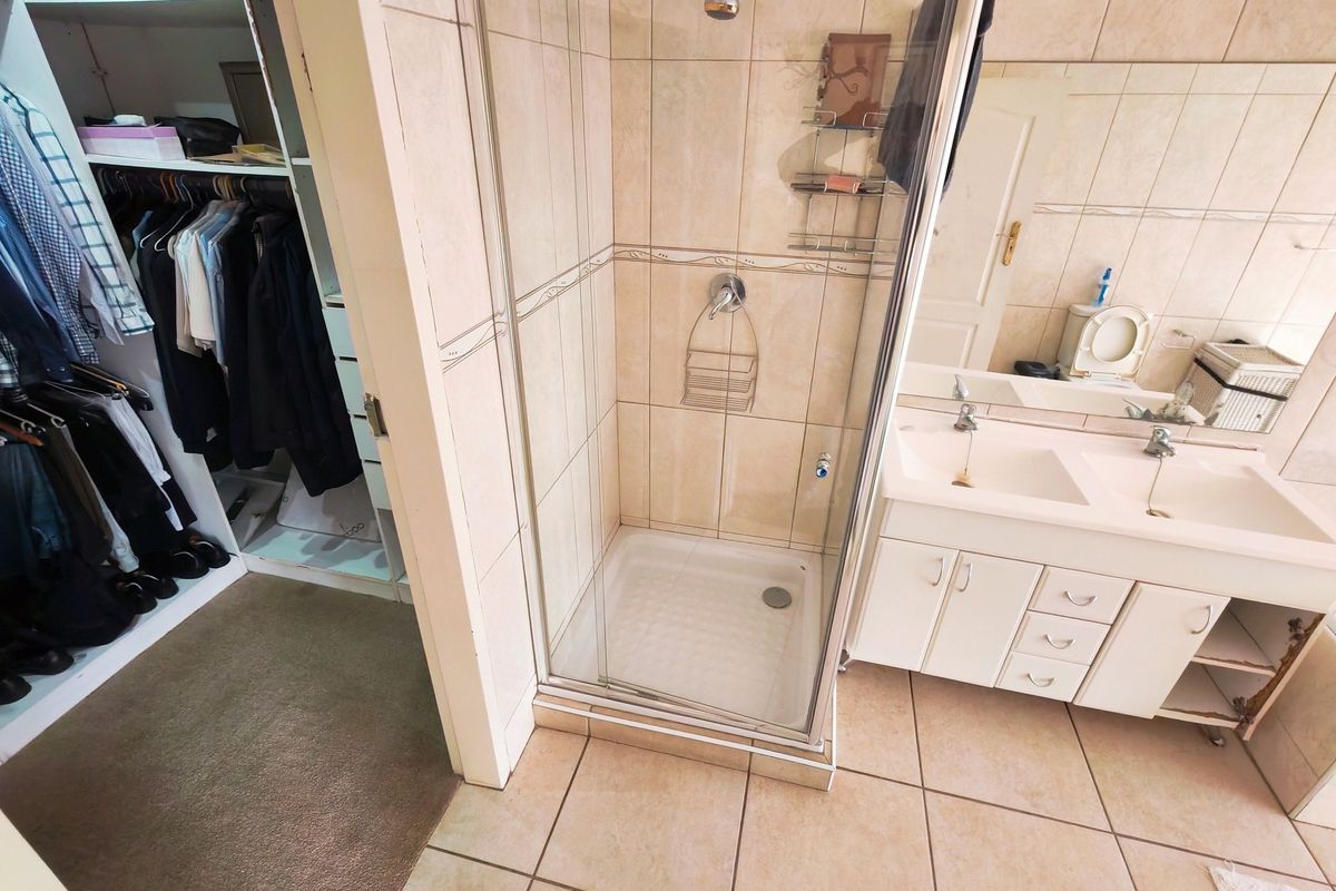 Bathroom featuring a shower enclosure, double vanity with storage, and adjacent walk-in closet with built-in shelving.