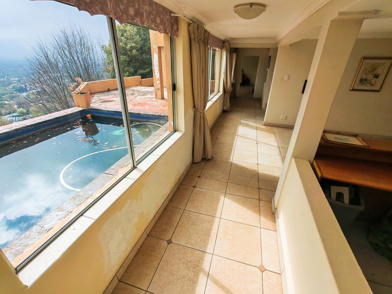 A sunlit hallway featuring tiled flooring and large windows overlooking an outdoor pool area, requiring cosmetic wall repairs and updates.