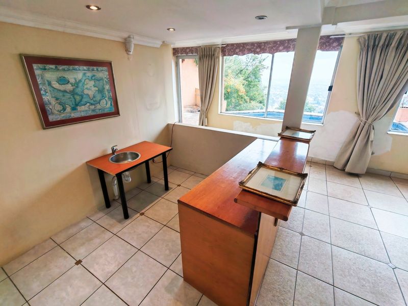 A bar area featuring a built-in counter, sink, tiled flooring, and large windows with views, requiring cosmetic wall repairs and updates.