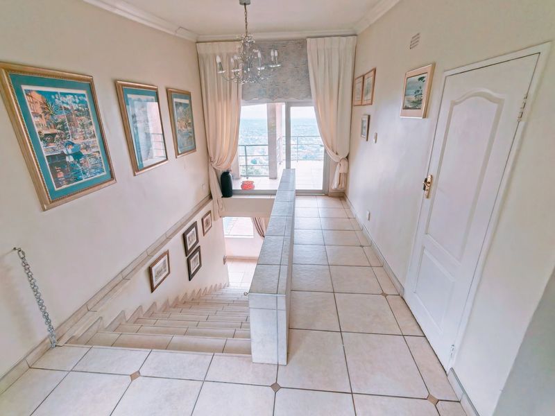 A bright, tiled hallway featuring a staircase with a tiled balustrade, leading towards a sliding glass door with views.