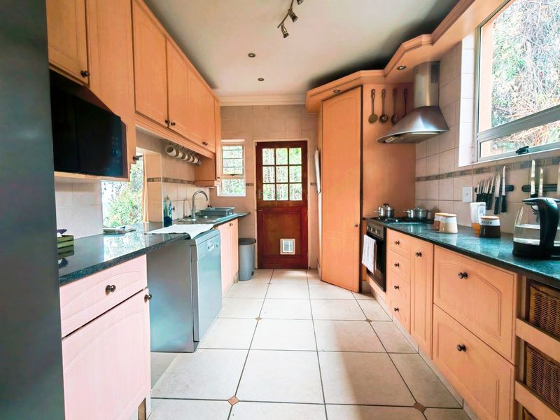 A functional kitchen featuring light wood cabinetry, stone countertops, tiled flooring, and integrated appliances, with direct access to the exterior via a timber door.