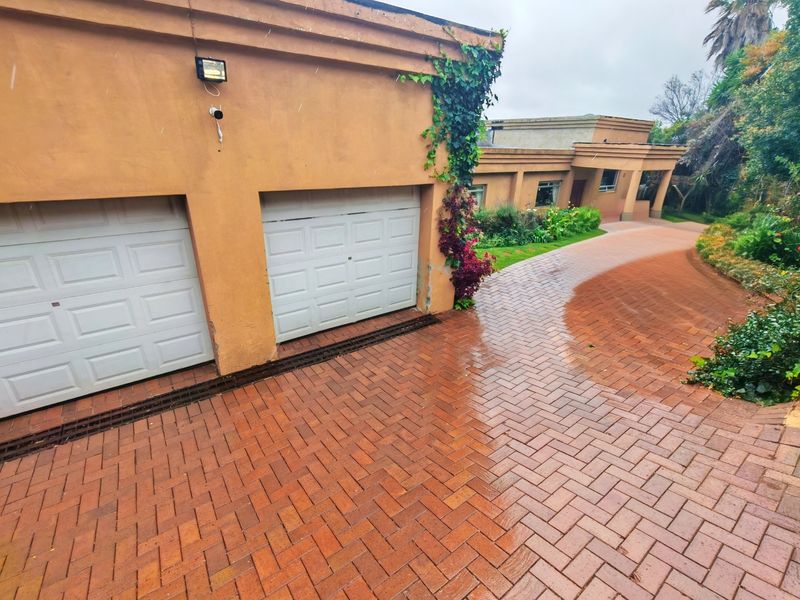 Front view of the property featuring a double garage, brick paved driveway, and established garden landscaping.