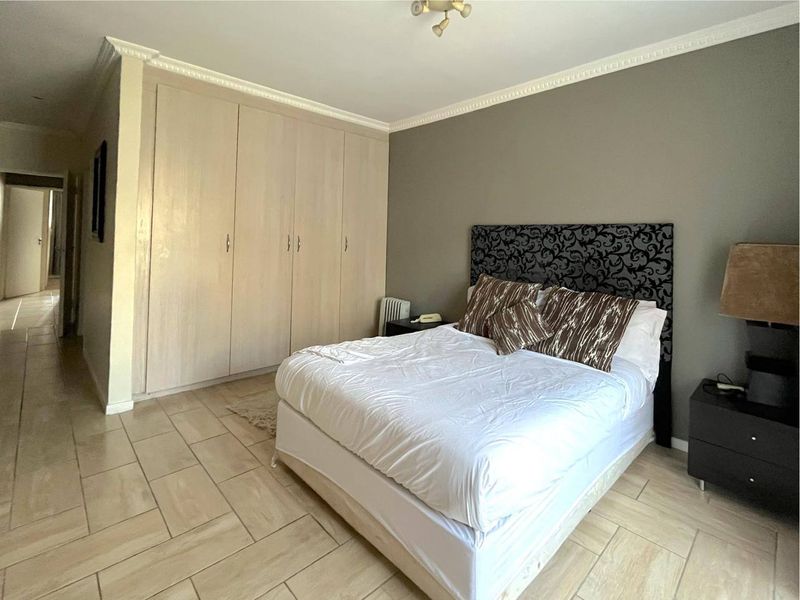 A bedroom featuring built-in cupboards, tiled flooring, and decorative crown molding, offering a functional and neutral living space.