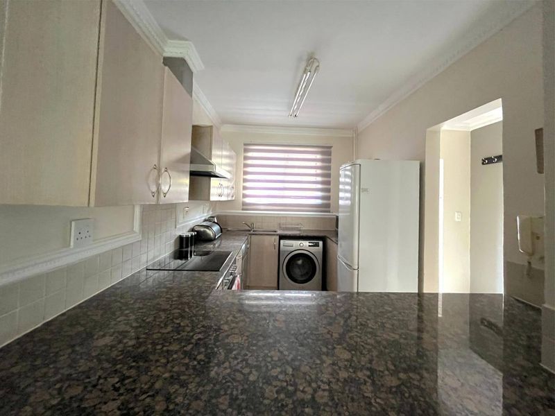 Functional kitchen featuring granite countertops, built-in cabinetry, an electric hob with extractor fan, and a tiled backsplash.