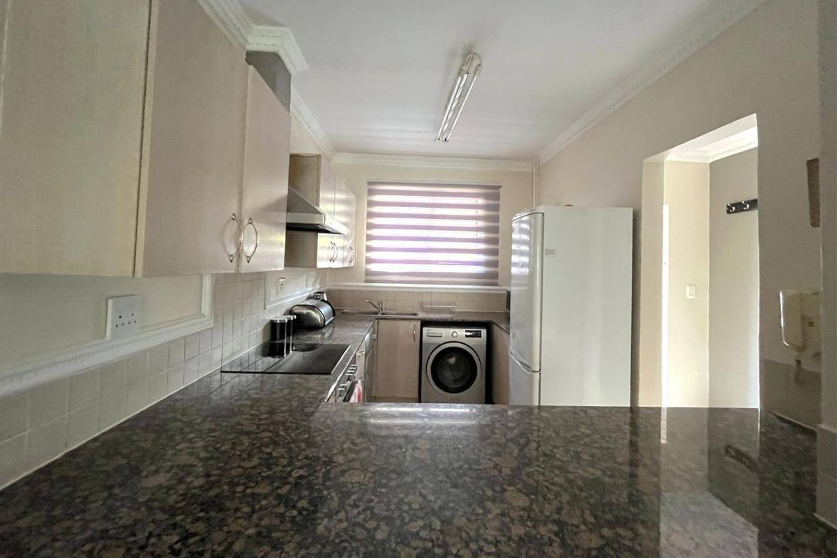 Functional kitchen featuring granite countertops, built-in cabinetry, an electric hob with extractor fan, and a tiled backsplash.
