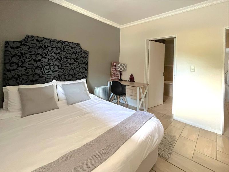 A well-maintained bedroom featuring tiled flooring, crown molding, and direct access to an en-suite bathroom.