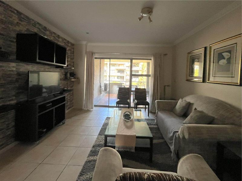 A living room featuring a stone-cladding accent wall, tiled flooring, and sliding glass doors providing access to an outdoor patio area.