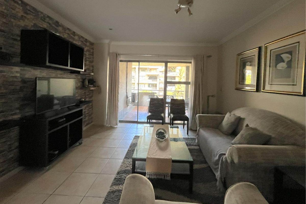 A living room featuring a stone-cladding accent wall, tiled flooring, and sliding glass doors providing access to an outdoor patio area.