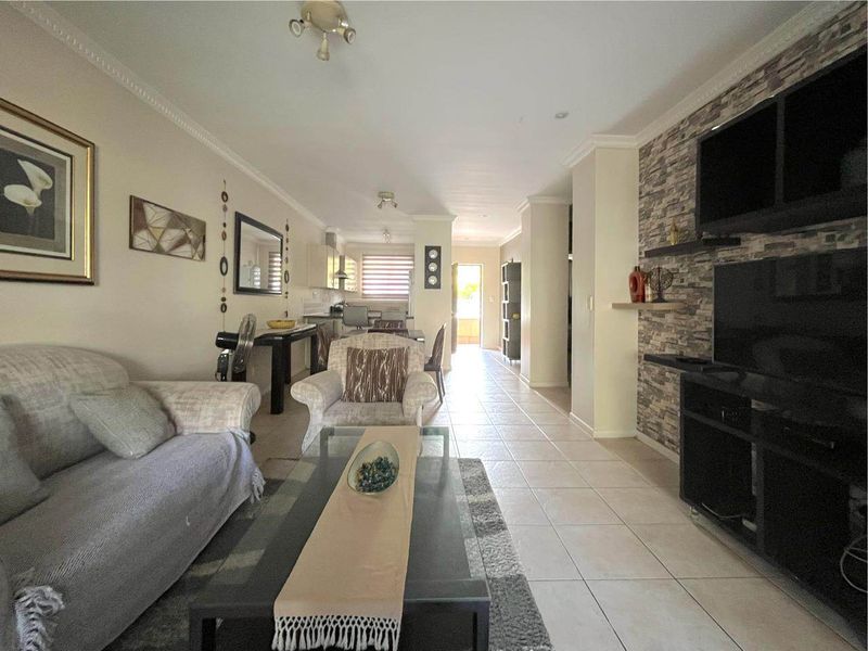 Open-plan living and kitchen area featuring tiled flooring, a stone feature wall, and crown molding, creating a functional and connected living space.