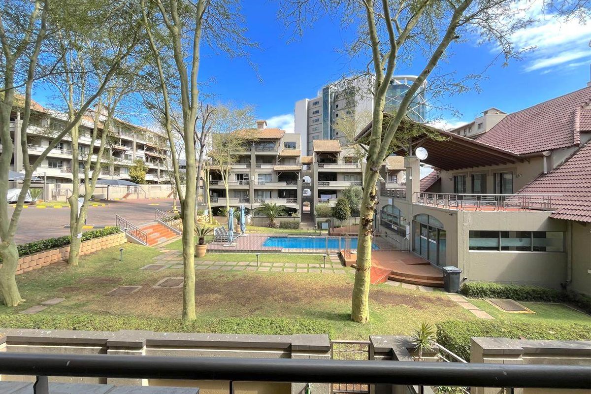 View of the apartment complex communal area featuring a swimming pool, landscaped garden, and paved walkways surrounded by multi-story residential buildings.