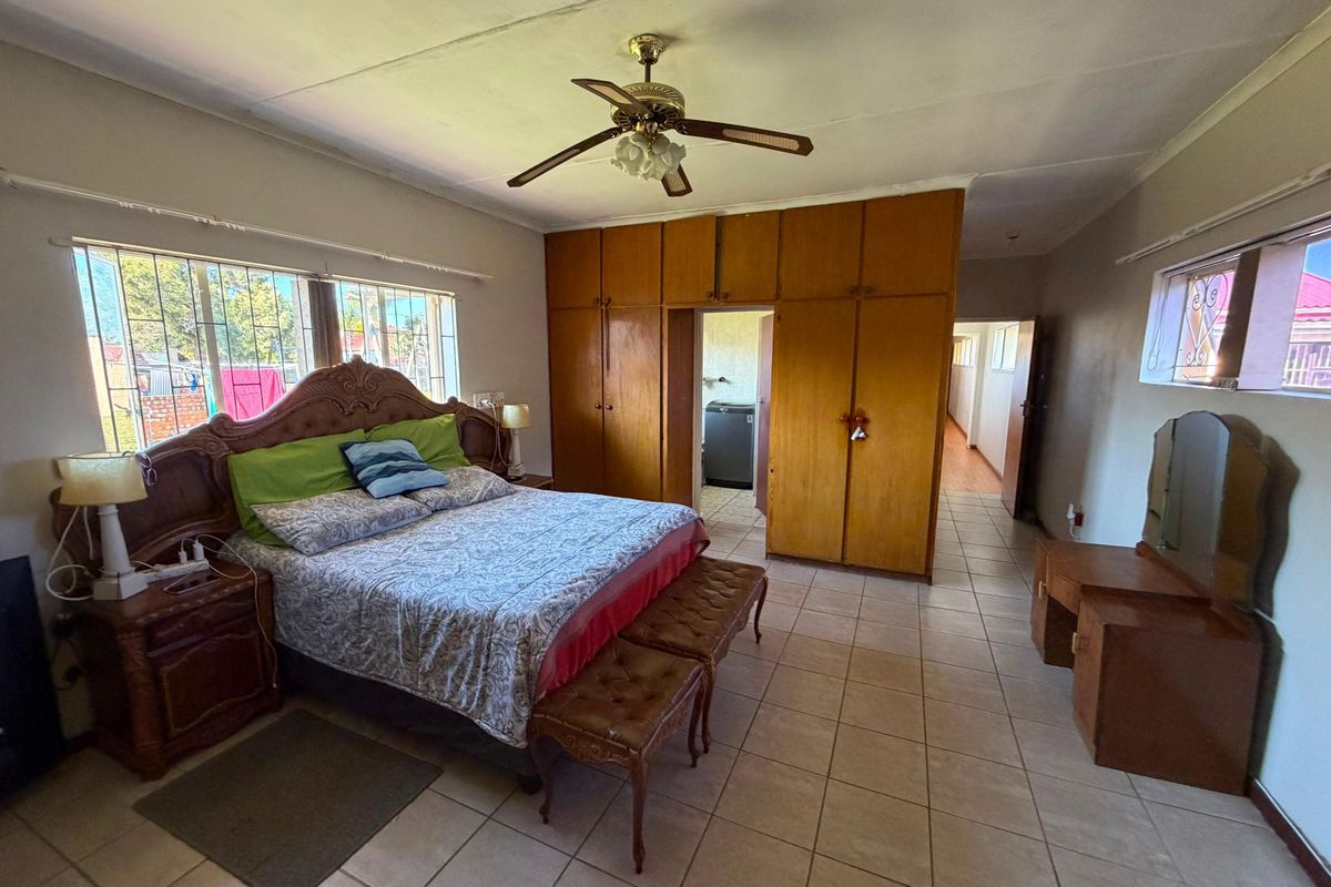Spacious bedroom featuring built-in wooden cupboards, tiled flooring, and a ceiling fan, offering a functional layout with direct access to an adjoining room.