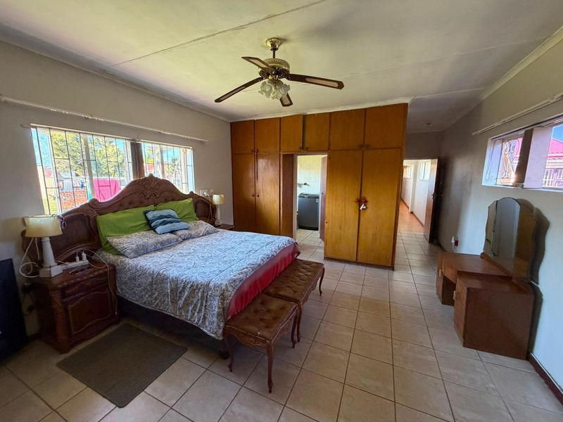 Spacious bedroom featuring built-in wooden cupboards, tiled flooring, and a ceiling fan, offering a functional layout with direct access to an adjoining room.