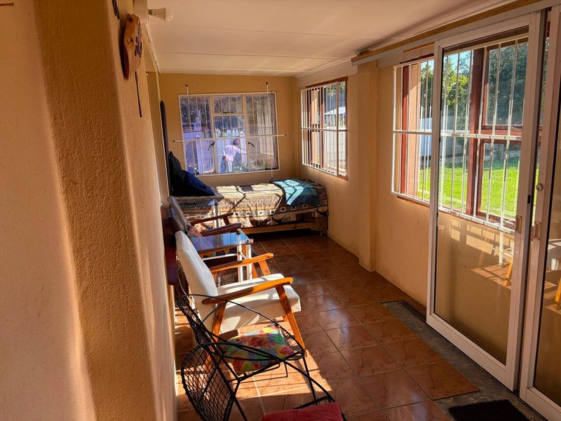 A sun-filled enclosed patio or sunroom featuring tiled flooring, large windows with security bars, and sliding glass door access to the garden.