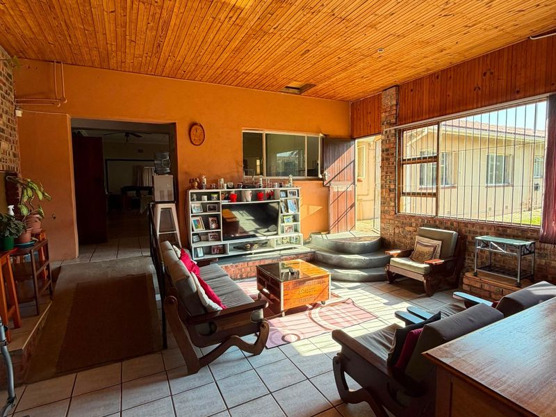 Spacious living area featuring a timber-clad ceiling, tiled flooring, and a brick feature wall with a built-in fireplace base.