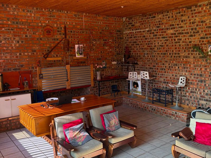 Spacious covered patio featuring exposed brick walls, a warm timber ceiling, and tiled flooring, offering a versatile area for relaxation or entertainment.