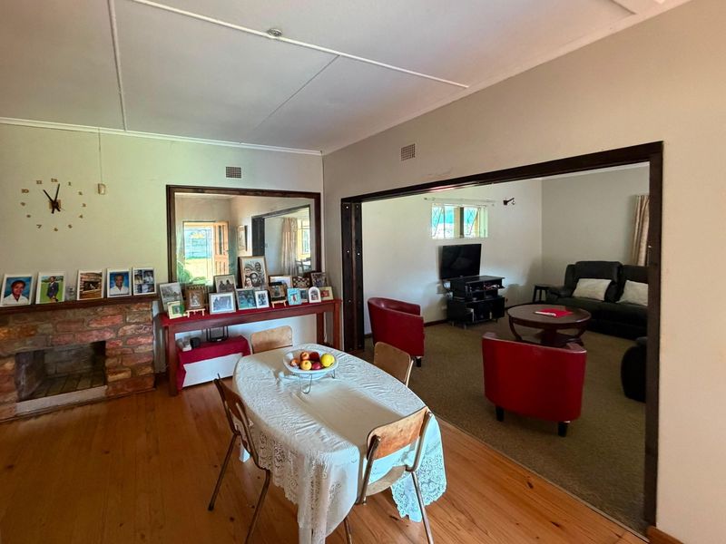 Open plan dining and living area featuring a brick fireplace, timber flooring, and a large wall mirror connecting to the adjacent lounge space.