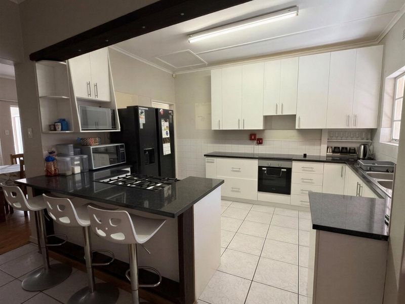 A functional kitchen featuring white cabinetry, dark granite countertops, a gas hob, built-in oven, and a breakfast bar with tiled flooring.