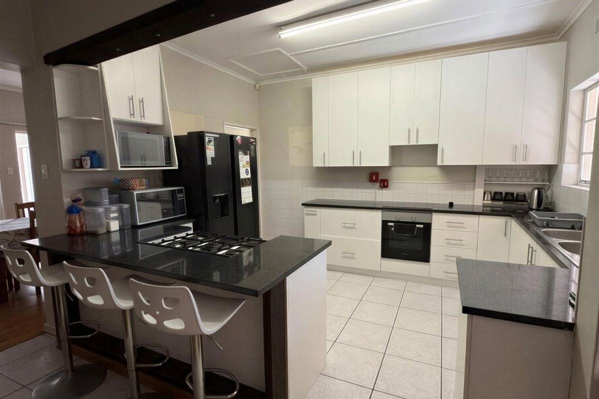 A functional kitchen featuring white cabinetry, dark granite countertops, a gas hob, built-in oven, and a breakfast bar with tiled flooring.