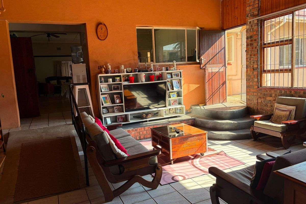 A sunlit living room featuring exposed brickwork, timber ceiling panels, and tiled flooring, with direct access to an outdoor area via a security door.