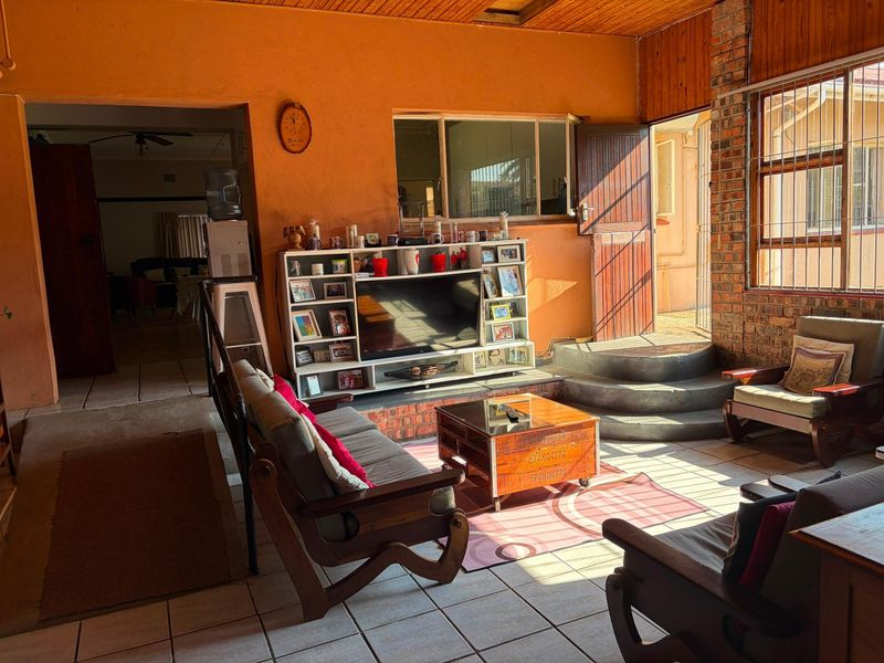 A sunlit living room featuring exposed brickwork, timber ceiling panels, and tiled flooring, with direct access to an outdoor area via a security door.