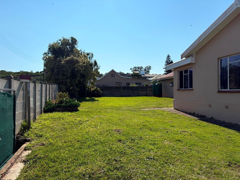 A spacious rear garden featuring a well-maintained lawn, a precast concrete boundary wall, and a water storage tank adjacent to the house exterior.