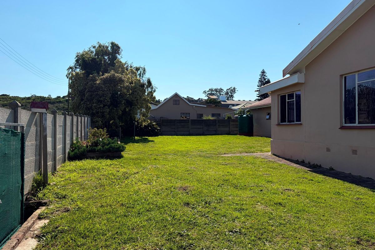 A spacious rear garden featuring a well-maintained lawn, a precast concrete boundary wall, and a water storage tank adjacent to the house exterior.