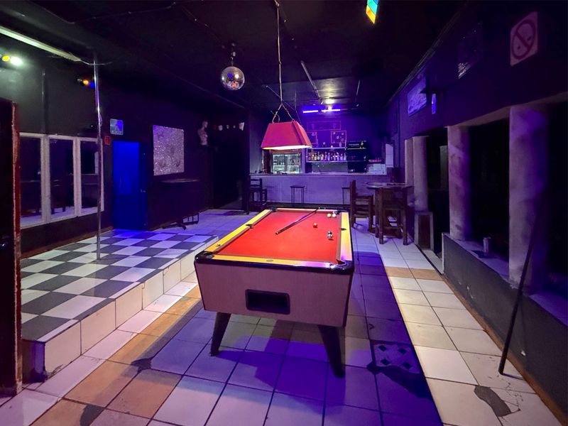 Commercial bar area featuring a built-in service counter, a raised stage with a dance pole, and tiled flooring throughout.