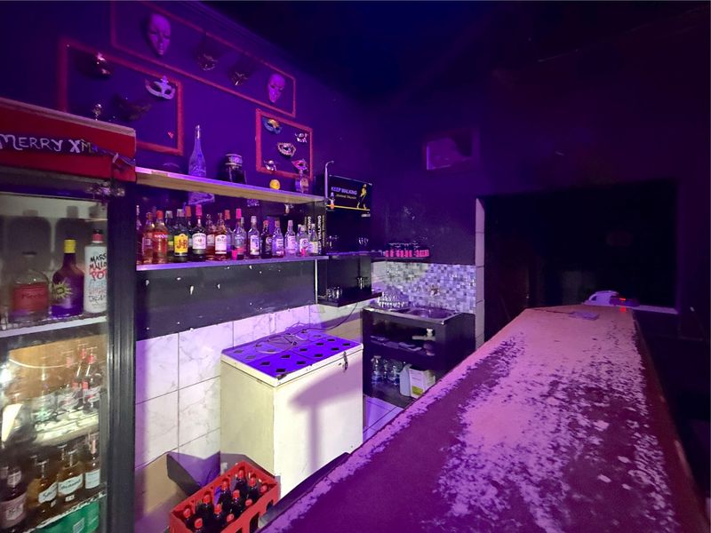A commercial bar area featuring a built-in counter, tiled splashback, and integrated sink, currently showing significant wear and dated finishes.